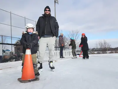 man and child on outdoor skating rink, child holding pylon