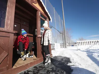 man tying skates in warming hut, with woman standing in skates at hut entrance