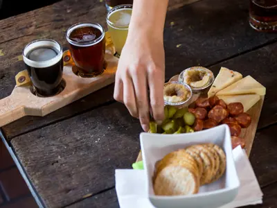 hand grabbing food from charcuterie board with flight of taster beers