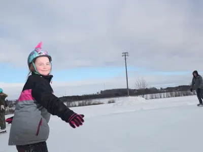 child skating on outdoor ice pad smiling at camera