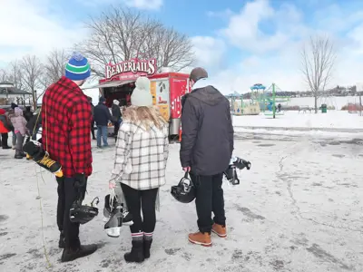 photo from behind of three people standing in parking lot, holding skating equipment, looking at Beavertails food truck