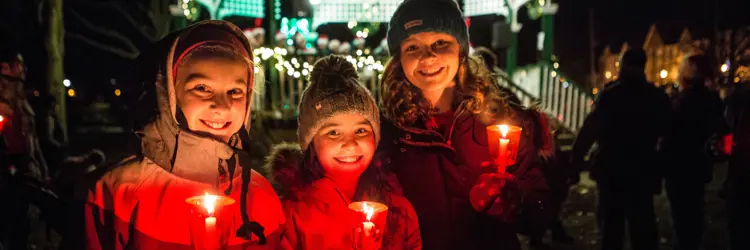 Three children holding candles at night in front of Palmer Park gazebo