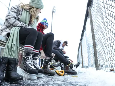 three people sitting on outdoor bench tying up skates