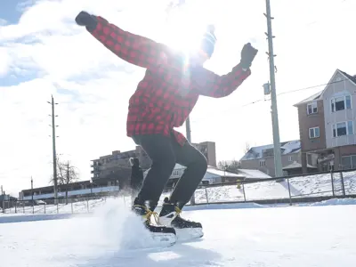 man stopping on outdoor skating rink with snow flying off skate blades