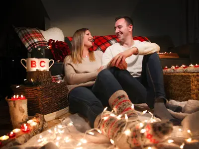 couple sitting in room with couch, blankets, string lighting, and coffee mugs